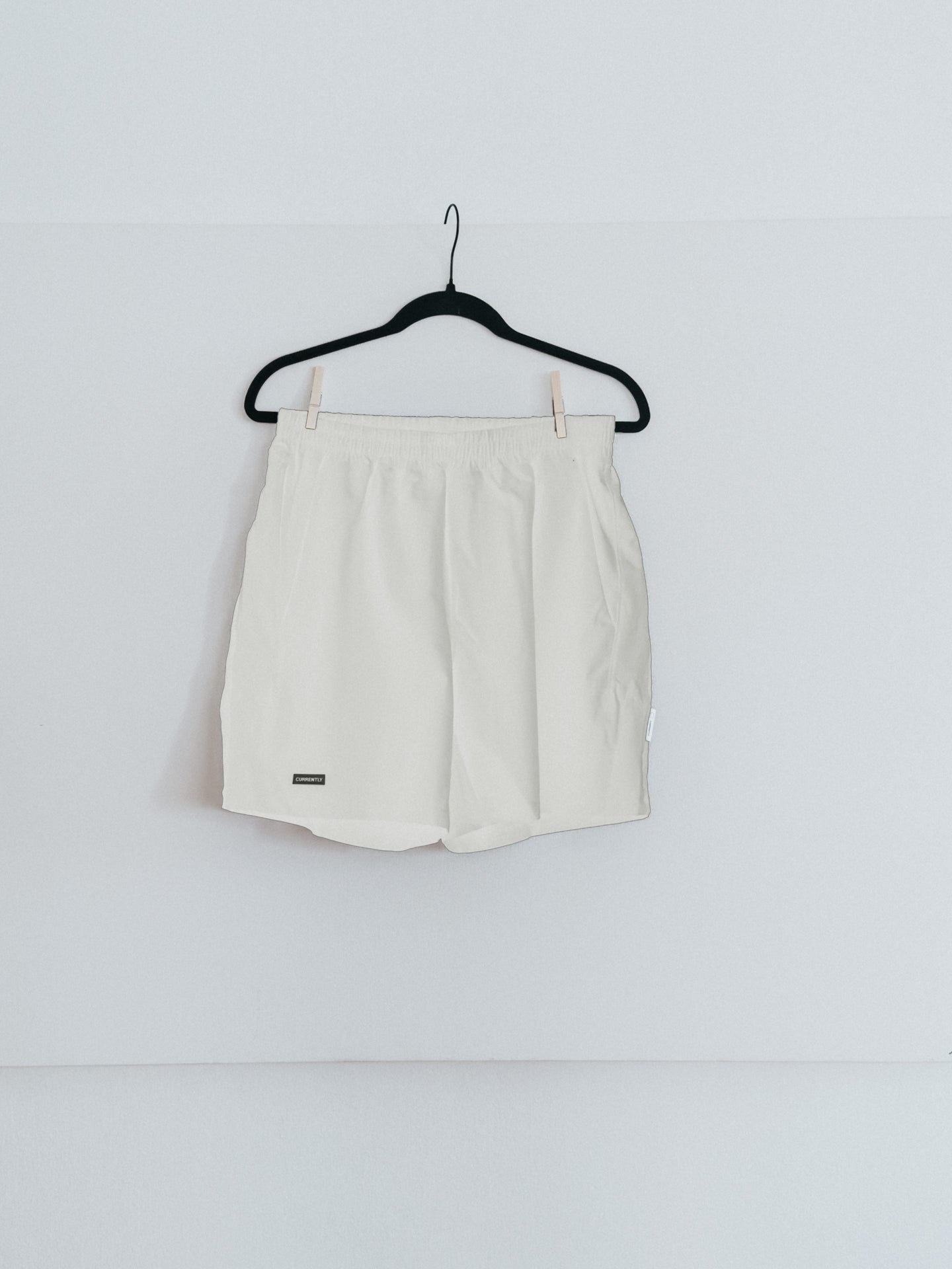 A pair of white running shorts hanging on a hanger against a plain wall.